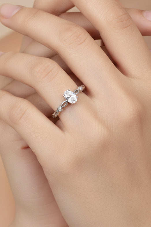 A silver ring with a small clear gemstone and a decorative textured band, shown on a plain light gray background with a small green tag attached.