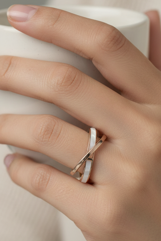 An interlocking double-band ring with a rose gold finish and a small green accent stone, photographed on a clean white reflective surface.
