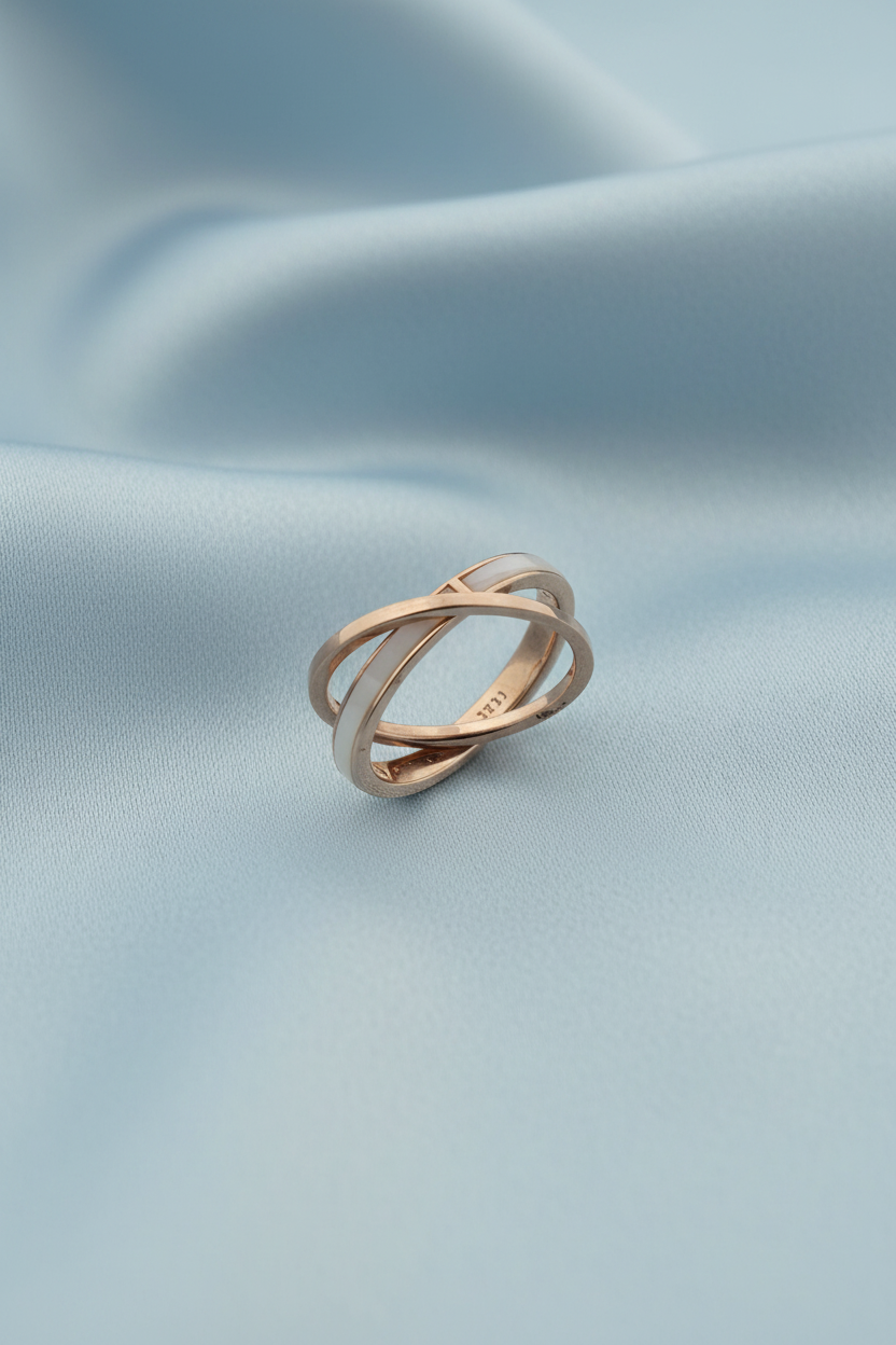 An interlocking double-band ring with a rose gold finish and a small green accent stone, photographed on a clean white reflective surface.