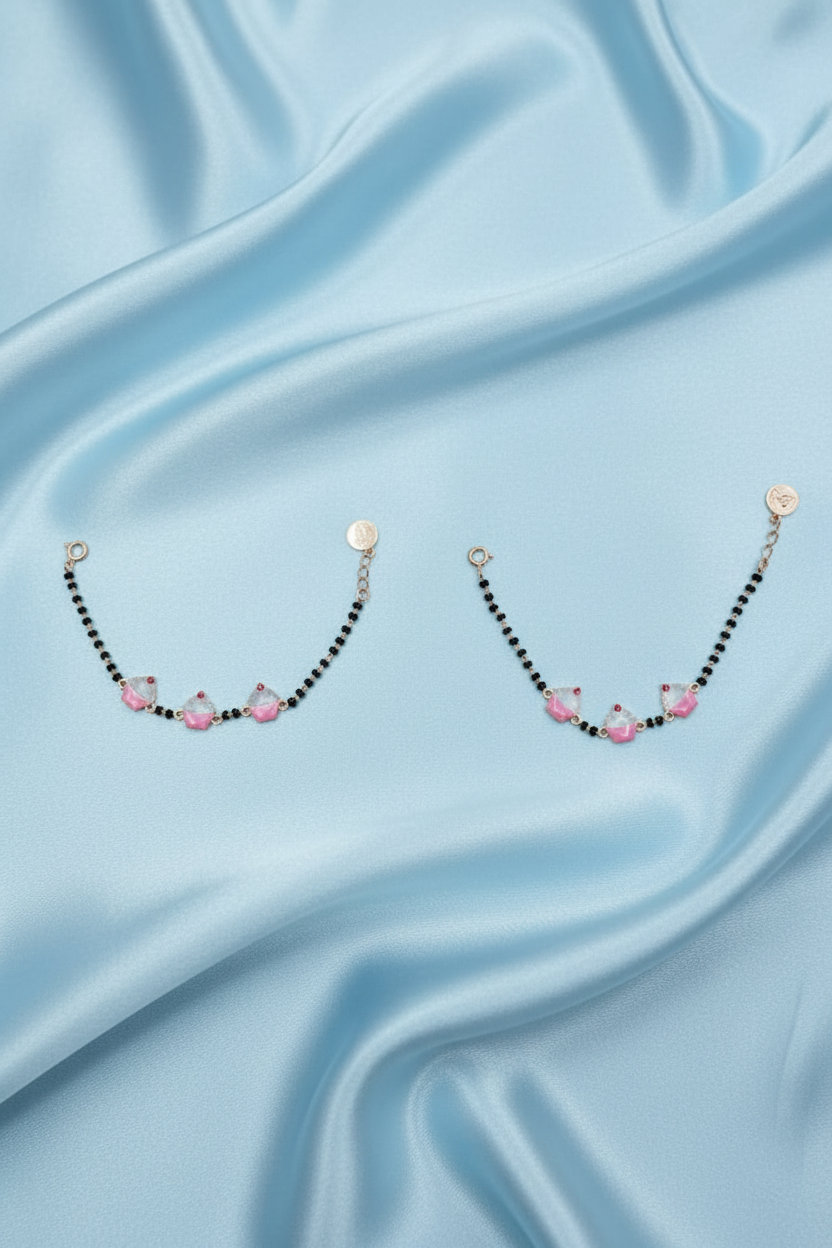 A pair of delicate rose gold chain bracelets with small black beads and pink floral accents, displayed on a light gray background.