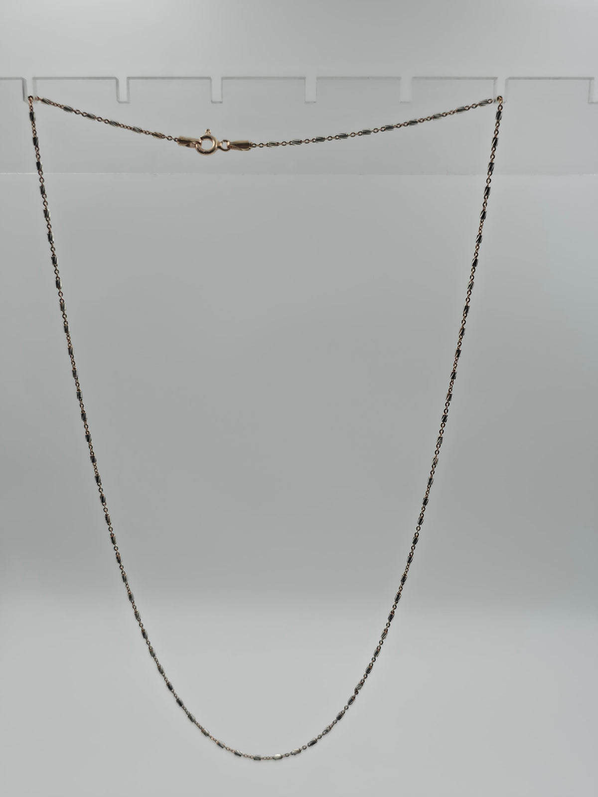 A delicate gold chain necklace with a small ring clasp, displayed against a neutral gray background.
